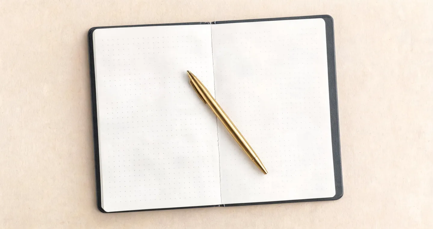 Top-down studio shot of an A5 hardcover dotted Leuchtturm1917 notebook with a Drehgriffel Nr. 1 ballpoint pen aligned on a beige paper backdrop
